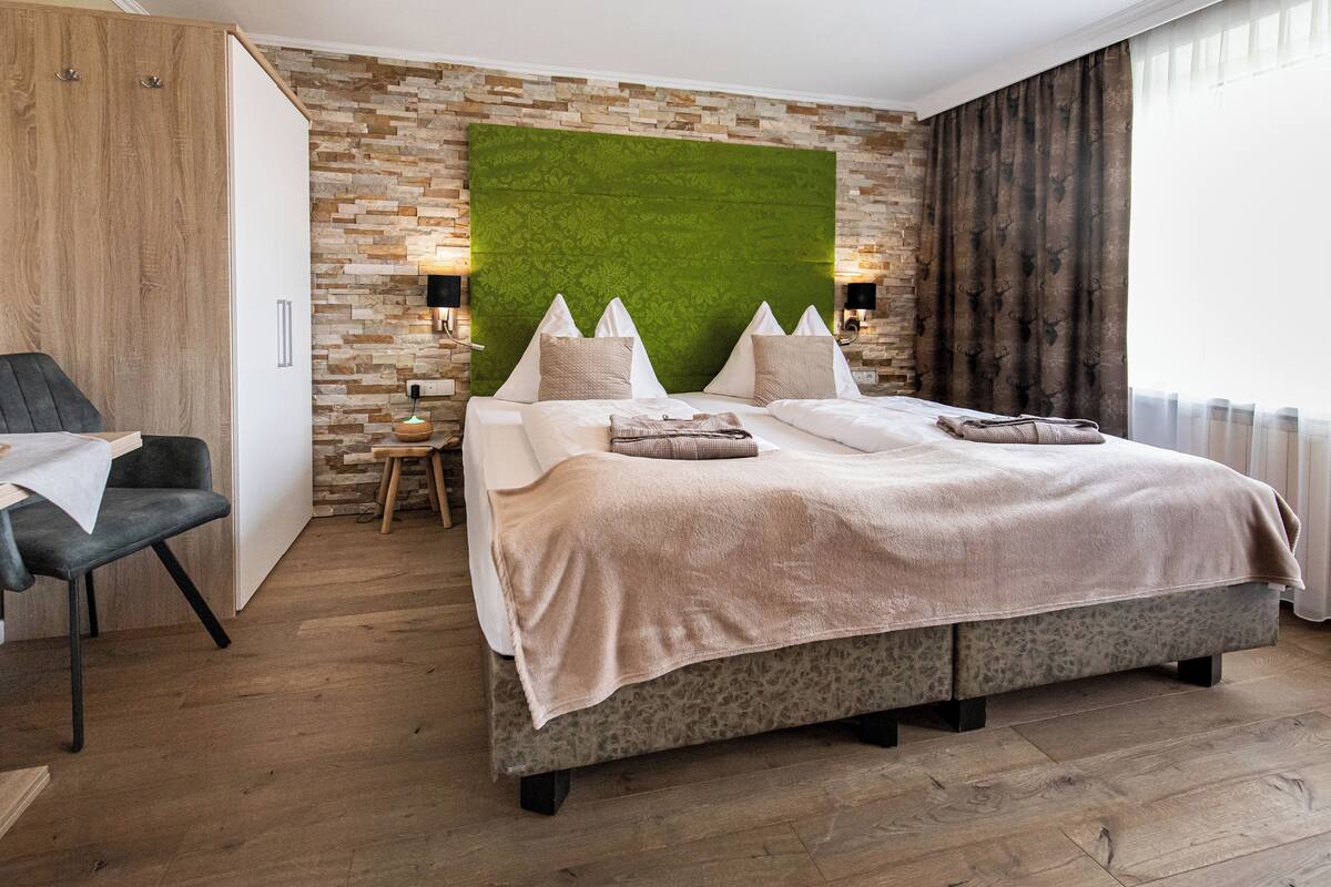 Een moderne slaapkamer met een groot bed, een houten garderobe, een klein tafeltje en een groene accentmuur.