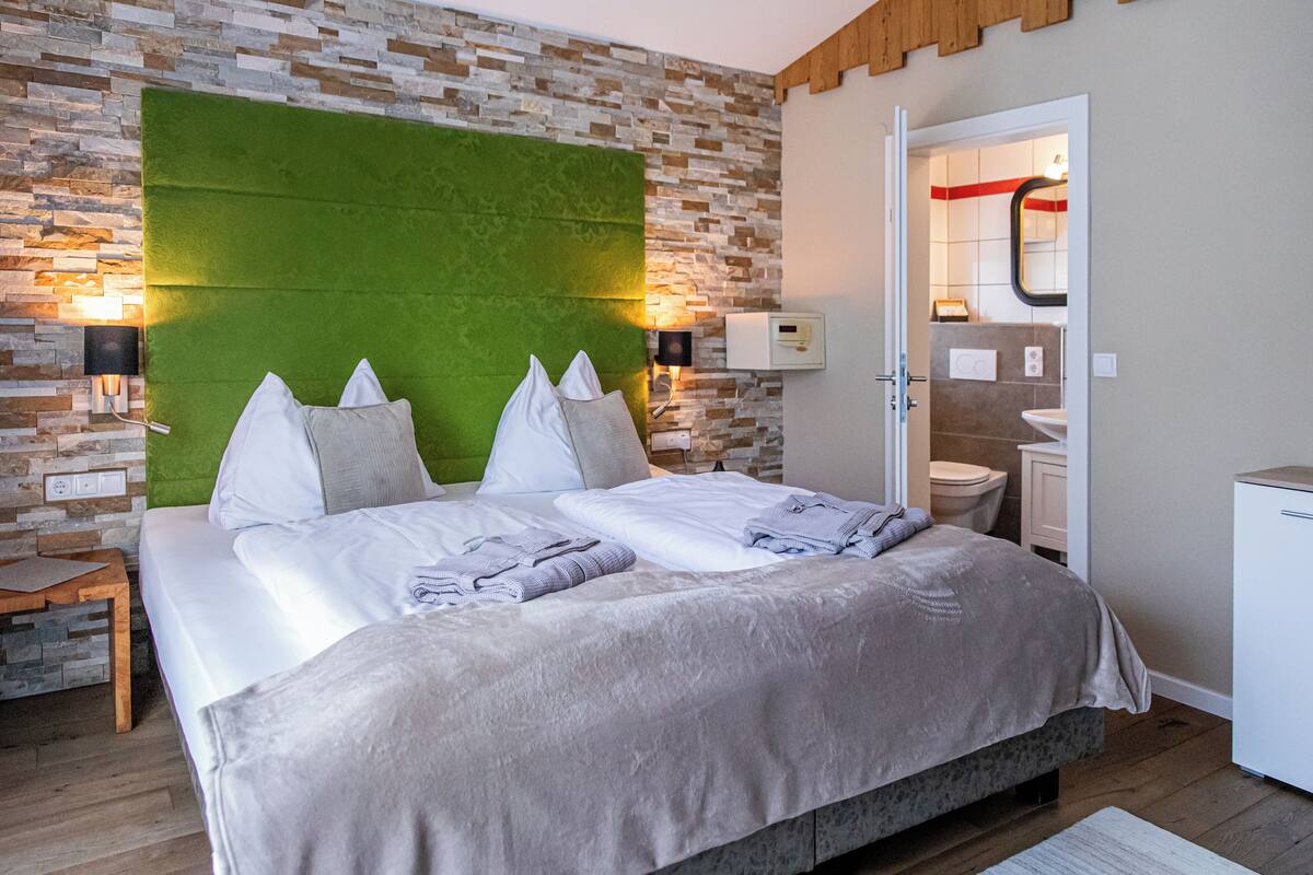 Een moderne hotelkamer met een groot bed, een groen hoofdeinde en een stenen muur.