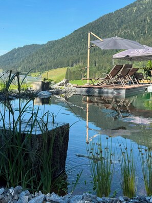 Vista al lago con muelle para botes, sillas de descanso y una terraza de madera.