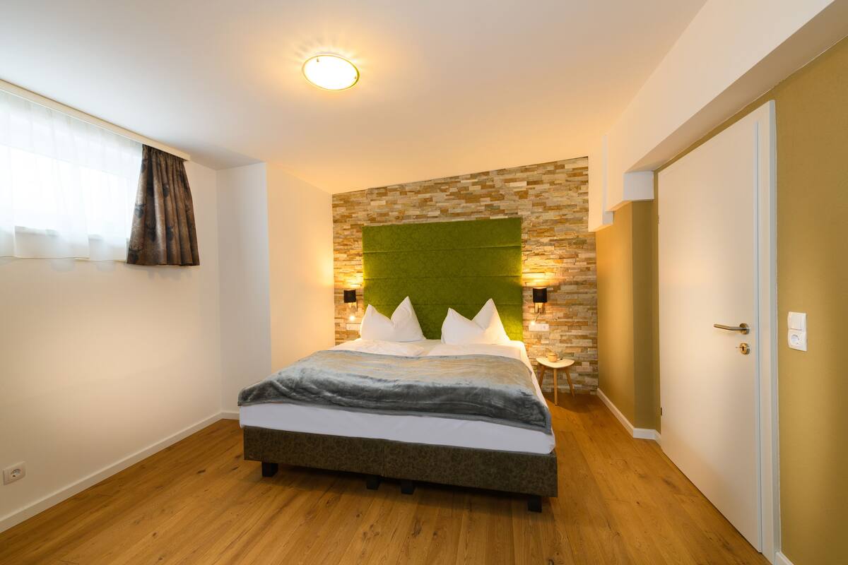 Een slaapkamer met een bed, een groen hoofdeinde, een stenen muur en een houten vloer.