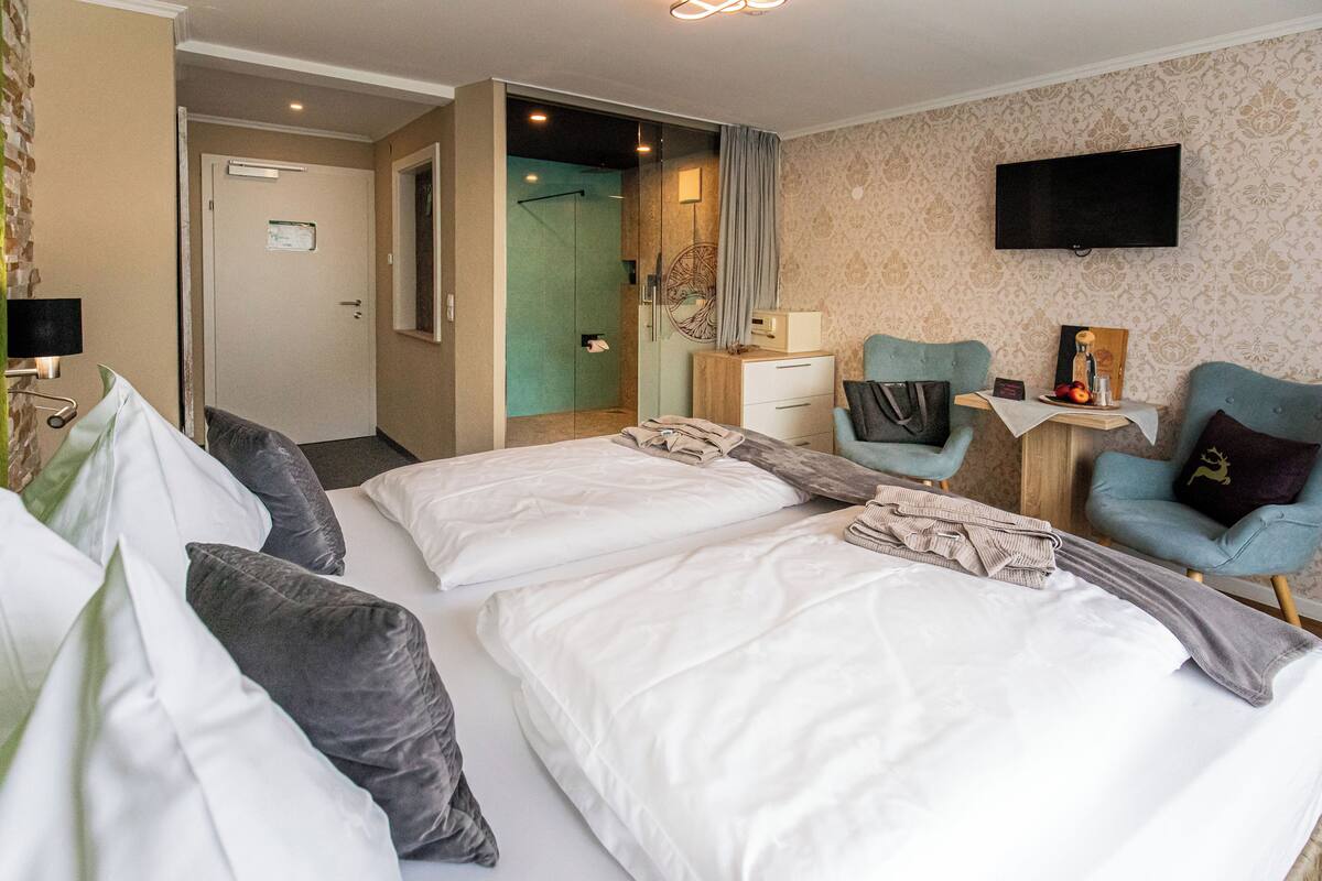 Een hotelkamer met twee bedden, een bureau, een stoel, een televisie en een douchehoek.