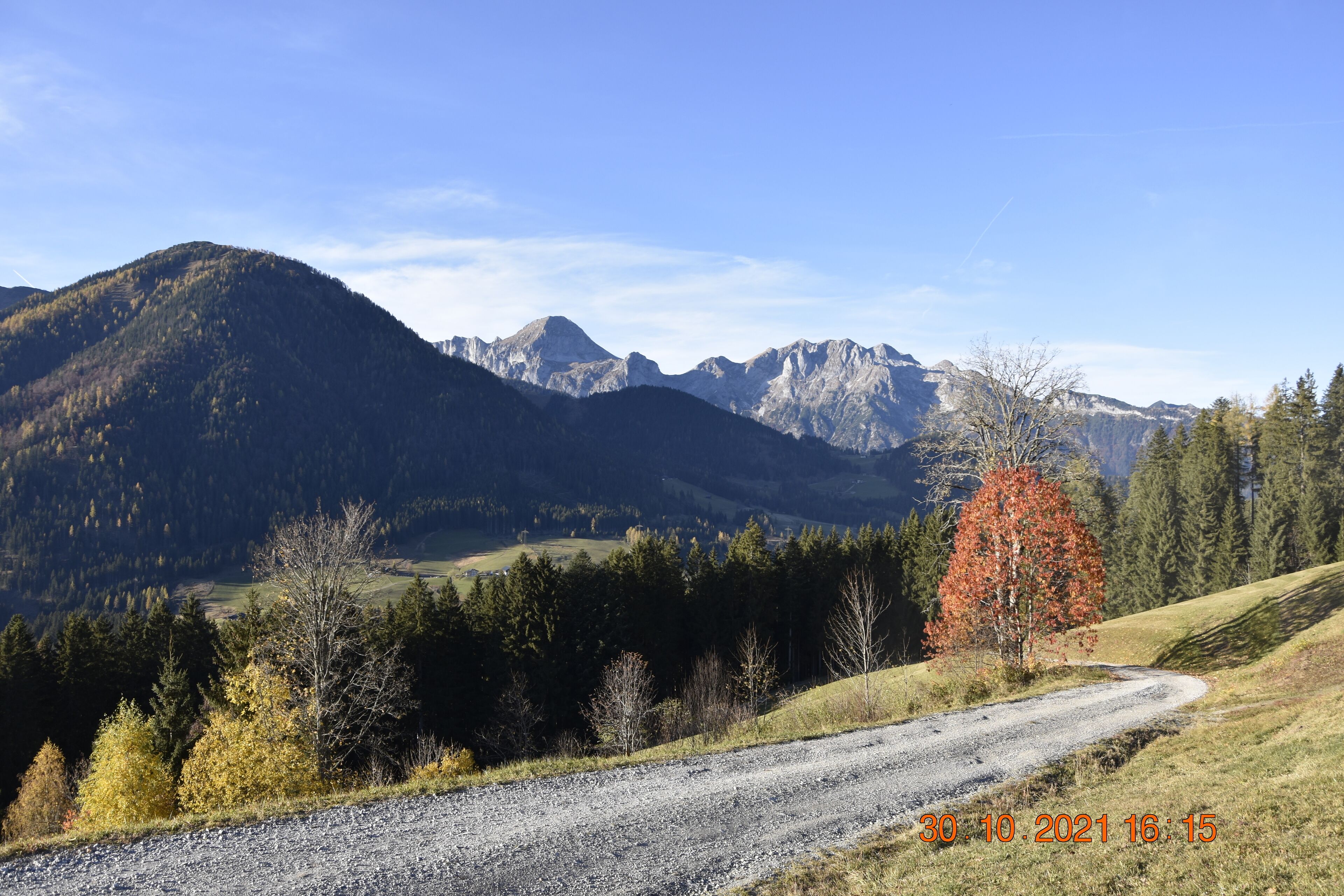 A gravel road winding through a mountainous landscape with autumn foliage and distant peaks.