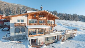 A large wooden chalet with multiple balconies, a covered terrace, and a ski slope in the background.