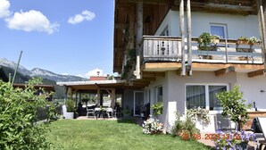 A chalet with a wooden balcony, a patio with outdoor furniture, and a view of mountains.