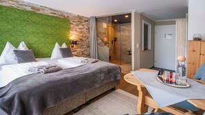 A modern bedroom with a green textured wall, a bed with grey bedding, a wooden table with a tray of glasses, and a wooden chair.