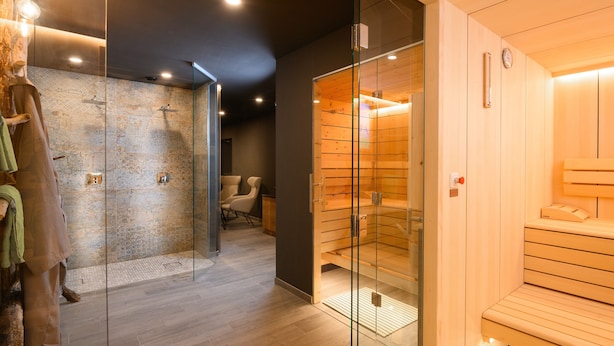 A modern sauna room with glass walls, wooden benches, and a stone wall.