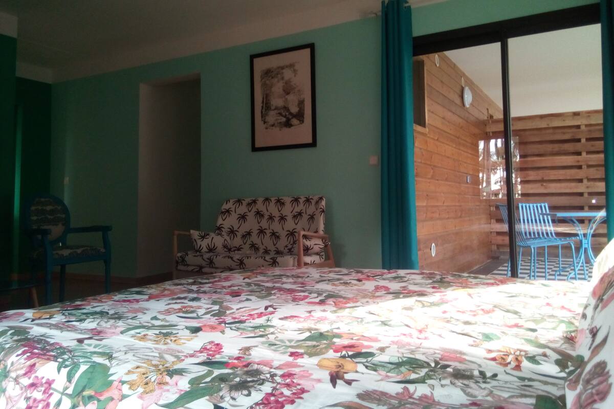 A room with a bed, a sofa, and a chair. There is a window with a view of the outside.