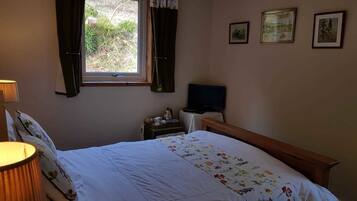 A bedroom with a bed, a bedside table with a lamp, a TV, and a window with curtains.