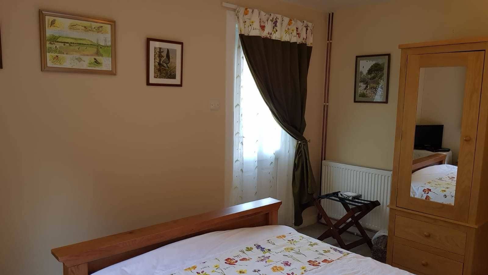 A bedroom with a wooden bed, a wooden dresser, a chair, and a window with curtains.