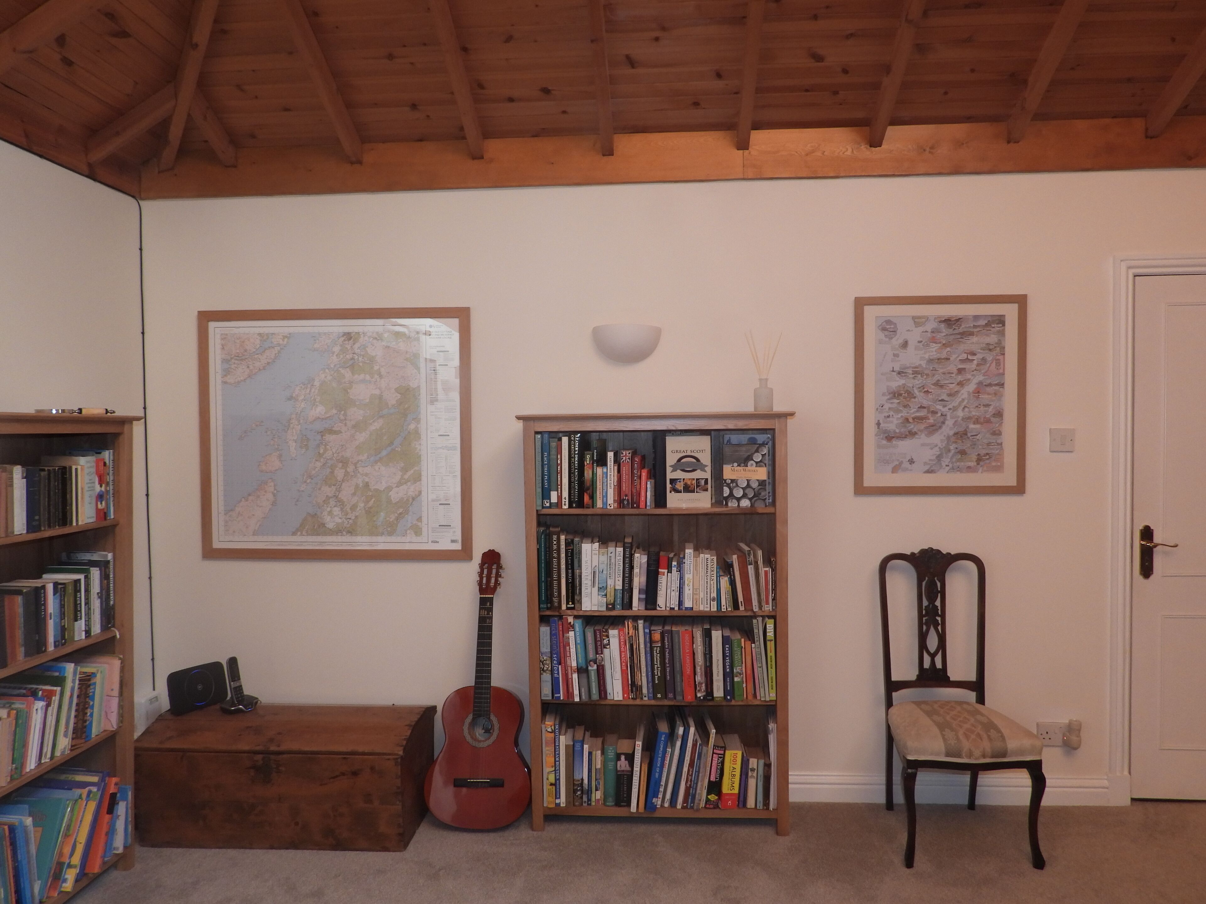 A room with a wooden ceiling, a bookshelf, a guitar, a map, and a chair.