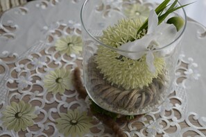 A clear glass vase with dried flowers and green foliage on a lace tablecloth. - Hotel Dreyer (Bad Rothenfelde)