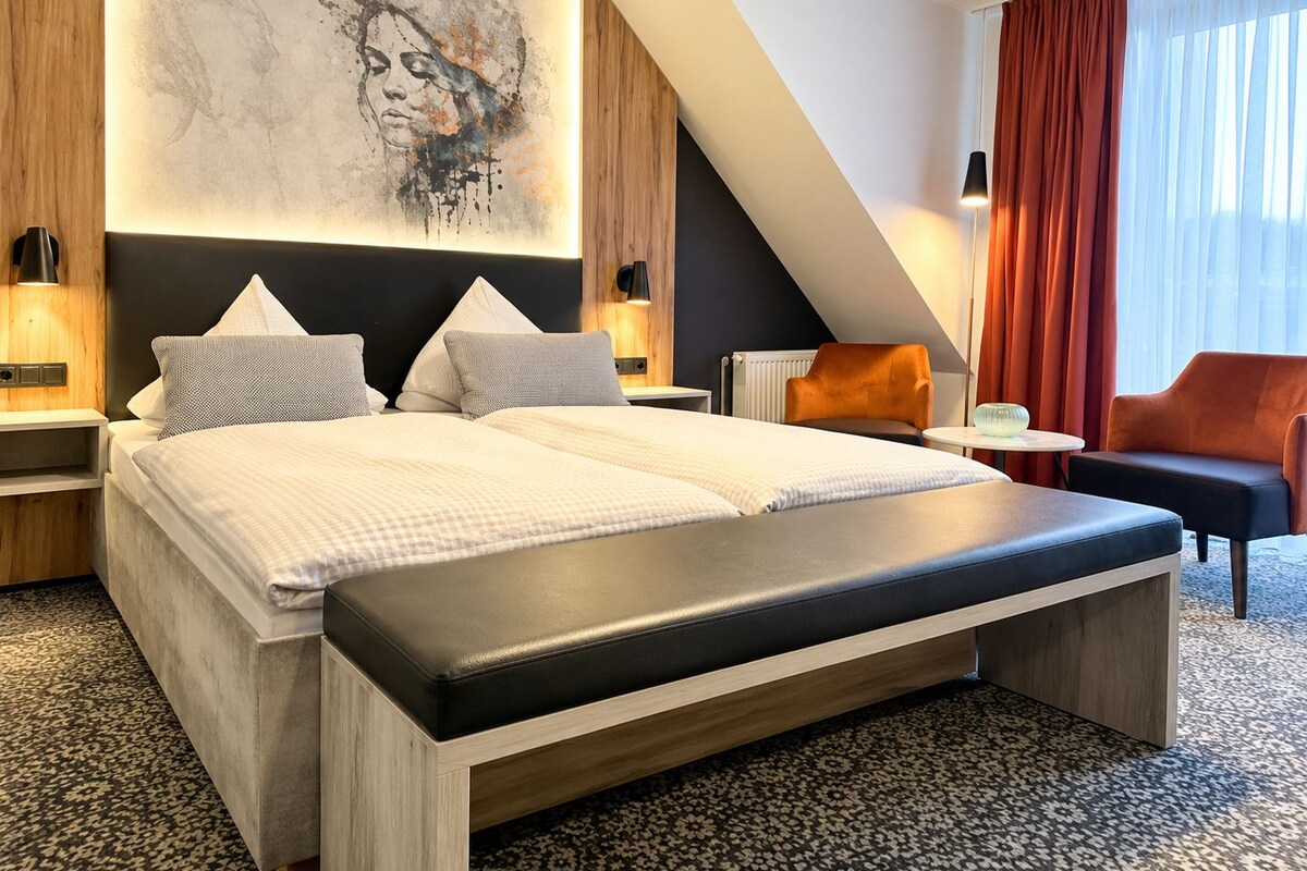 A modern hotel room with a large bed, a bench, a desk, and a chair.