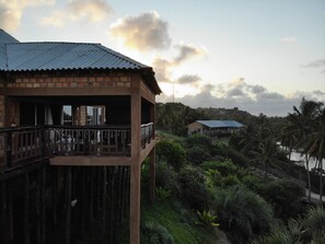 A wooden building with a balcony overlooking a lush landscape with palm trees and a distant house. - Gin and Jack Beach House (Inhambane)
