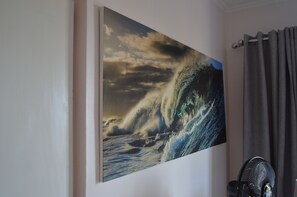 A room with a large painting of a wave on the wall, a black fan, and a curtain. - Gin and Jack Beach House (Inhambane)