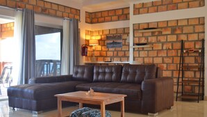 A modern living room with a brown leather sofa, a wooden coffee table, and a brick wall. - Gin and Jack Beach House (Inhambane)