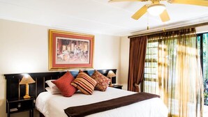 Ein Hotelzimmer mit einem großen Bett, einem Deckenventilator, einem gerahmten Bild an der Wand und einem Fenster mit Vorhängen.