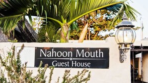Schild für das Nahoon Mouth Guest House mit Straßenlaterne und tropischen Pflanzen.