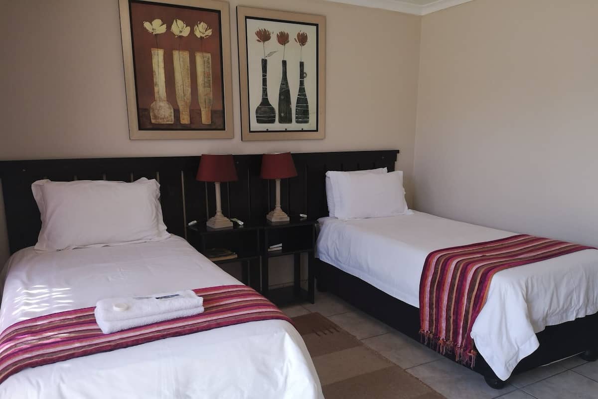 Ein Hotelzimmer mit zwei Einzelbetten, weißer Bettwäsche, einer gestreiften Decke, zwei Nachttischen mit Lampen und zwei gerahmten Bildern an der Wand.