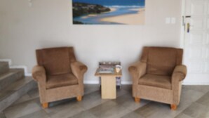 Ein Zimmer mit zwei Sesseln, einem kleinen Tisch und einem Strandbild an der Wand.