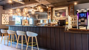 Una zona de bar con taburetes, iluminación colgante, una barra y un espejo grande.