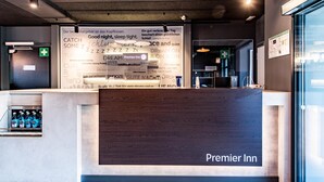 Un mostrador de recepción con un letrero de Premier Inn, una puerta de cristal y una pared con varios textos y símbolos.