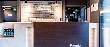 A reception desk with a sign for Premier Inn, a glass door, and a wall with various text and symbols.
