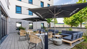 Un patio con mobiliario exterior, incluyendo sillas de mimbre y un sofá, bajo grandes sombrillas.