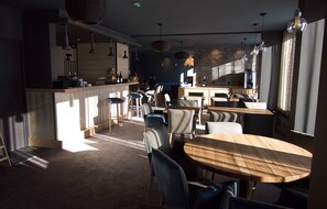 A modern restaurant with a bar area, wooden tables, and hanging pendant lights. - Alberta Hotel & Spa (Les Belleville)