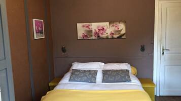 Ein Schlafzimmer mit einem Bett, einer gelben Decke, zwei Kissen mit Blumenmustern und einem Wandbild von rosa Blumen.