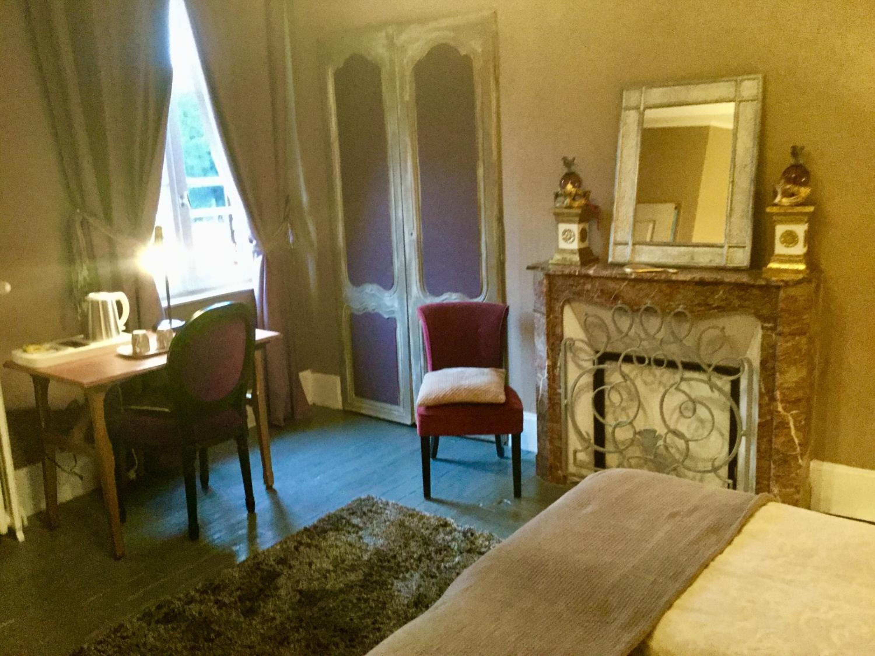 A hotel room with a bed, a desk with a chair, a fireplace, and a large mirror.