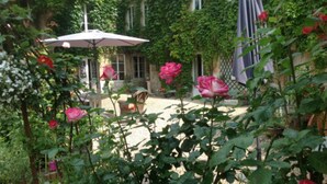 En have med terrasse, et bord og stole, omgivet af frodigt grønt og blomstrende planter.