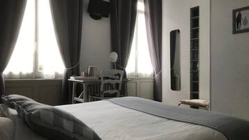 Een slaapkamer met een bed, een bureau, een stoel, een televisie en een raam met gordijnen.