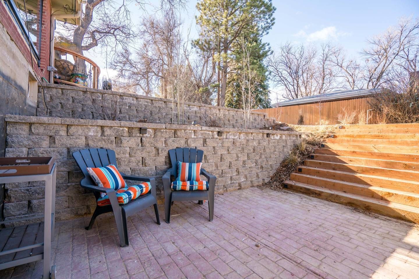A patio area with two Adirondack chairs, a stone wall, and a wooden staircase.
