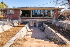 A two-story house with a brick exterior, a covered patio with outdoor seating, and a front door leading to a garage. - The Sophisticated Boho Escape Perfect for Two (Denver)
