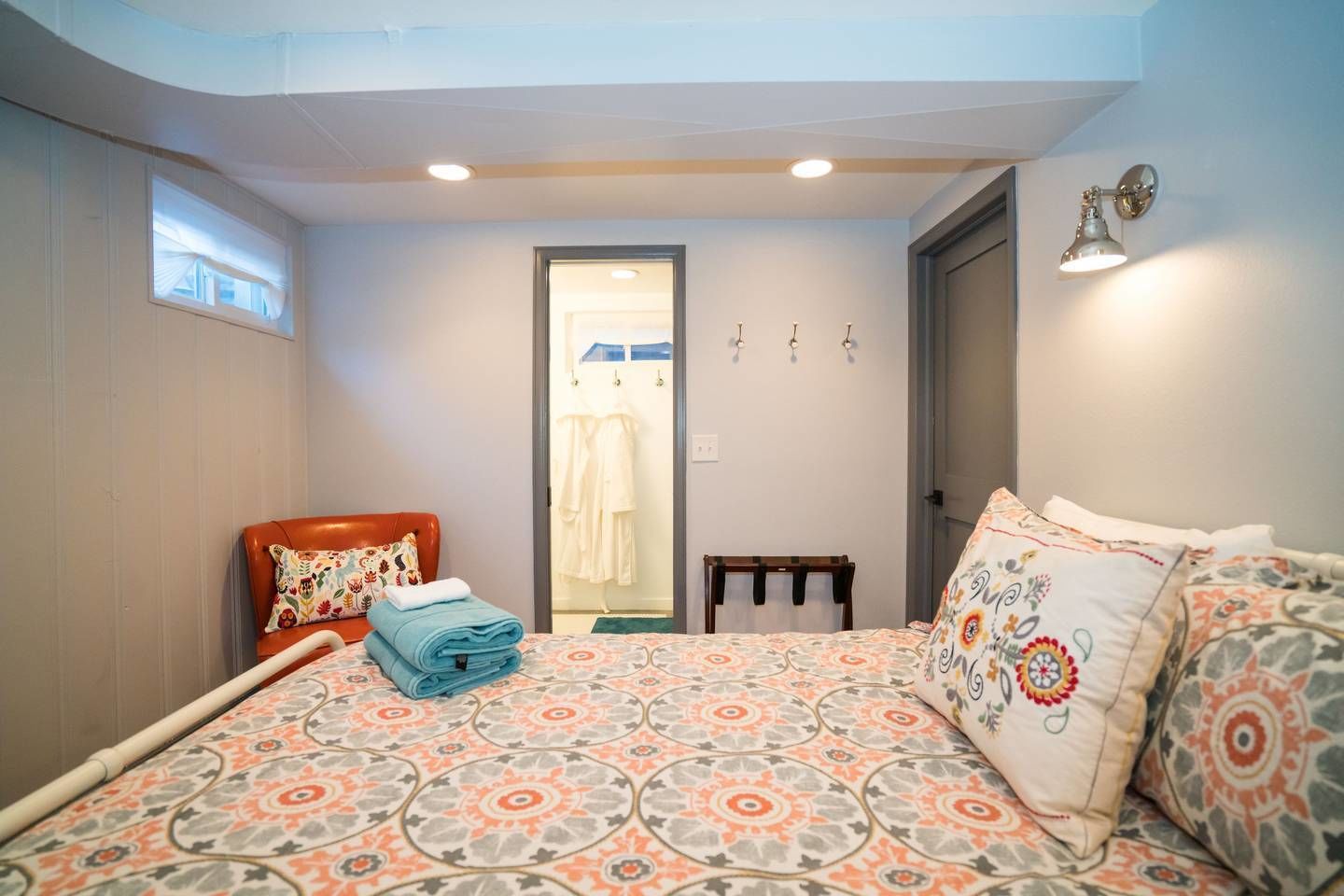 A bedroom with a bed, a chair, a small table, and a door leading to a bathroom.
