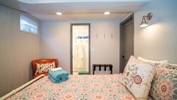 A bedroom with a bed, a chair, a small table, and a door leading to a bathroom.