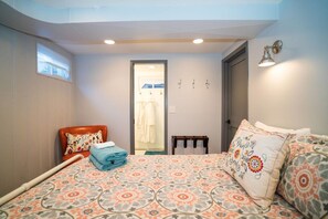 Un dormitorio con cama, una silla, una mesita y una puerta que da al baño.