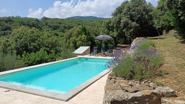 A rectangular swimming pool with a tiled edge, surrounded by a stone wall. There are lounge chairs and a covered area with a striped roof.