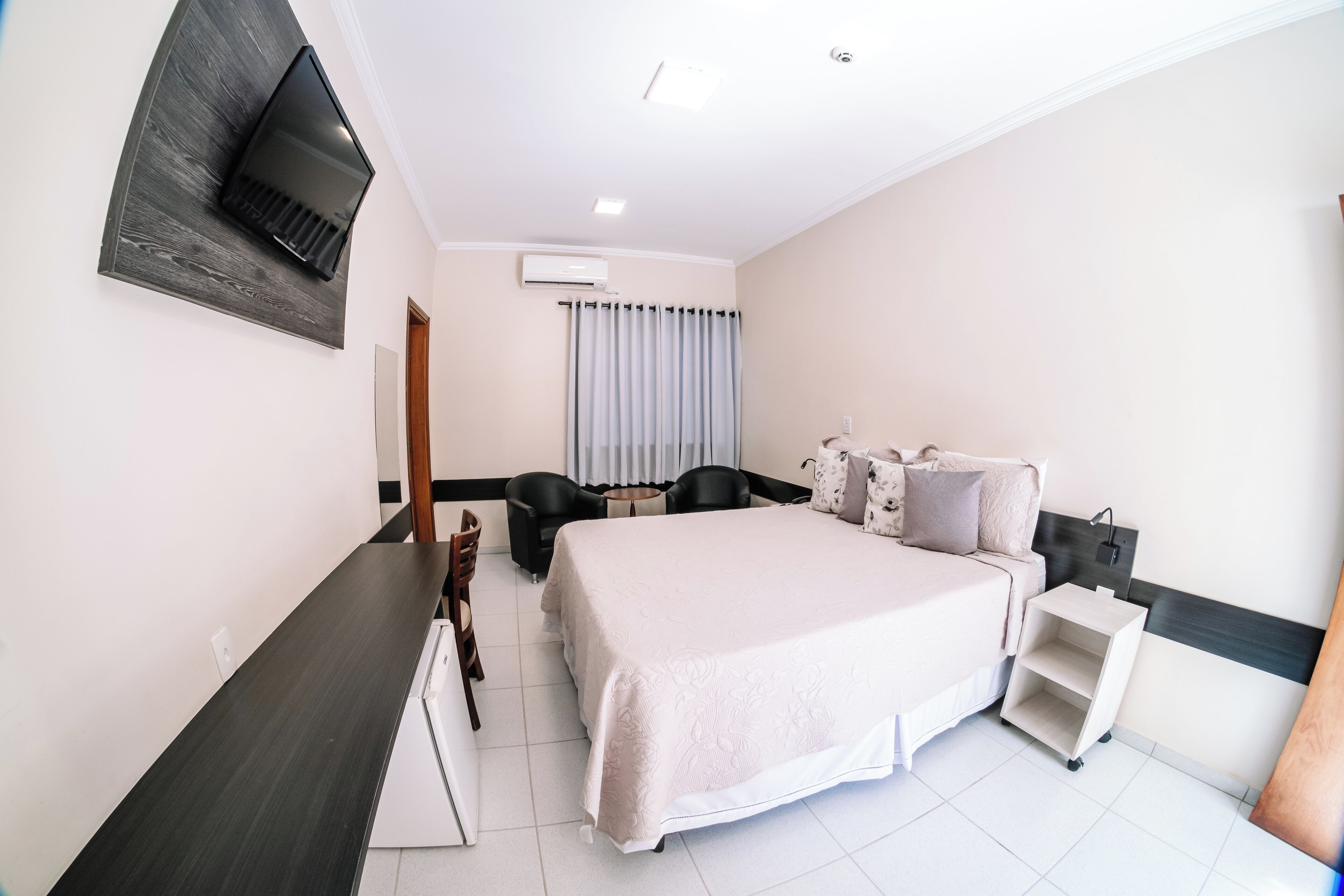 Une chambre d’hôtel équipée d’un lit, d’un bureau, d’une chaise, d’un téléviseur fixé au mur et d’une fenêtre avec des rideaux.