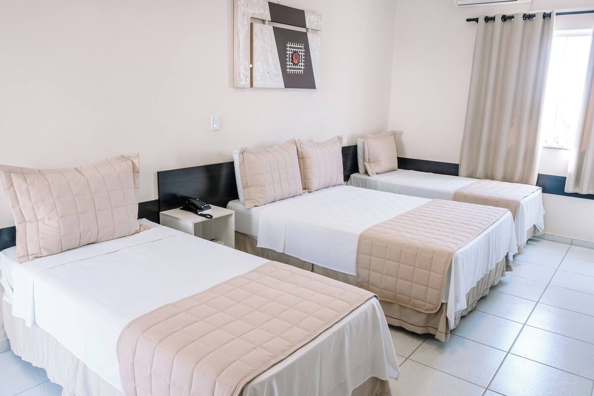 Une chambre d’hôtel avec trois lits, un téléviseur à écran plat et une fenêtre avec des rideaux.