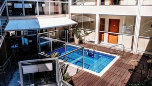 Un hotel de varios niveles con una piscina central, asientos al aire libre y un balcón con paredes de vidrio.