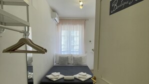 A hotel room with a bed, a mirror, a coat rack, a window with curtains, and a sign on the door. - Trastevere Sweet Rest (Rome)