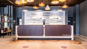 Un espace d’accueil d’hôtel au design moderne, comprenant un comptoir d’accueil, un éclairage suspendu et un mur orné de divers textes et logos.