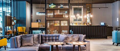 A modern lounge area with a sectional sofa, round tables, and a bar with shelves of bottles.