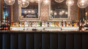 Un bar avec de nombreuses bouteilles d’alcool et des verres, des luminaires sphériques suspendus et un grand miroir.