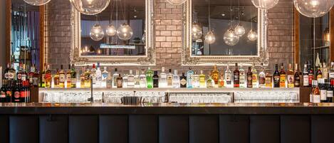 A bar with multiple liquor bottles and glasses, hanging spherical light fixtures, and a large mirror.