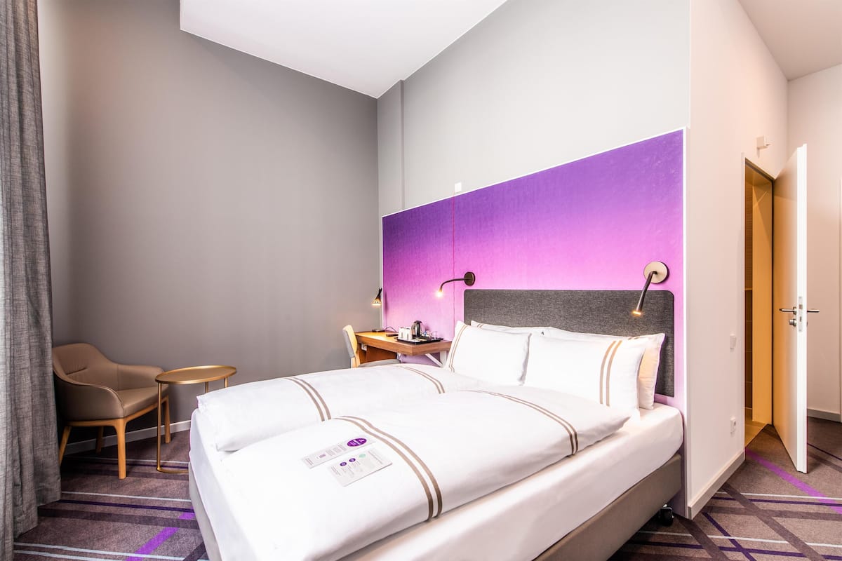 Ein Hotelzimmer mit Bett, Stuhl, kleinem Tisch und Schreibtisch mit Lampe.