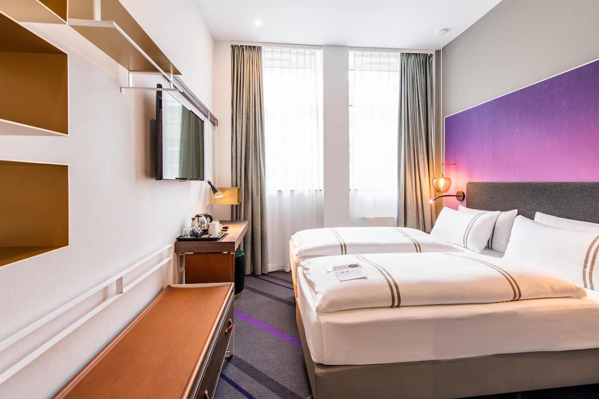 Ein Hotelzimmer mit Bett, Schreibtisch mit Lampe, Fernseher und einem Fenster mit Vorhängen.