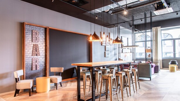 Un espace bar moderne avec une table en bois, des tabourets de bar, des luminaires suspendus et un mur décoratif en briques.