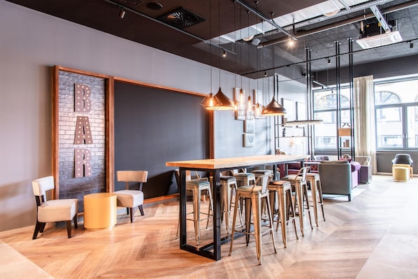 A modern bar area with a wooden table, bar stools, pendant lighting, and a brick accent wall.